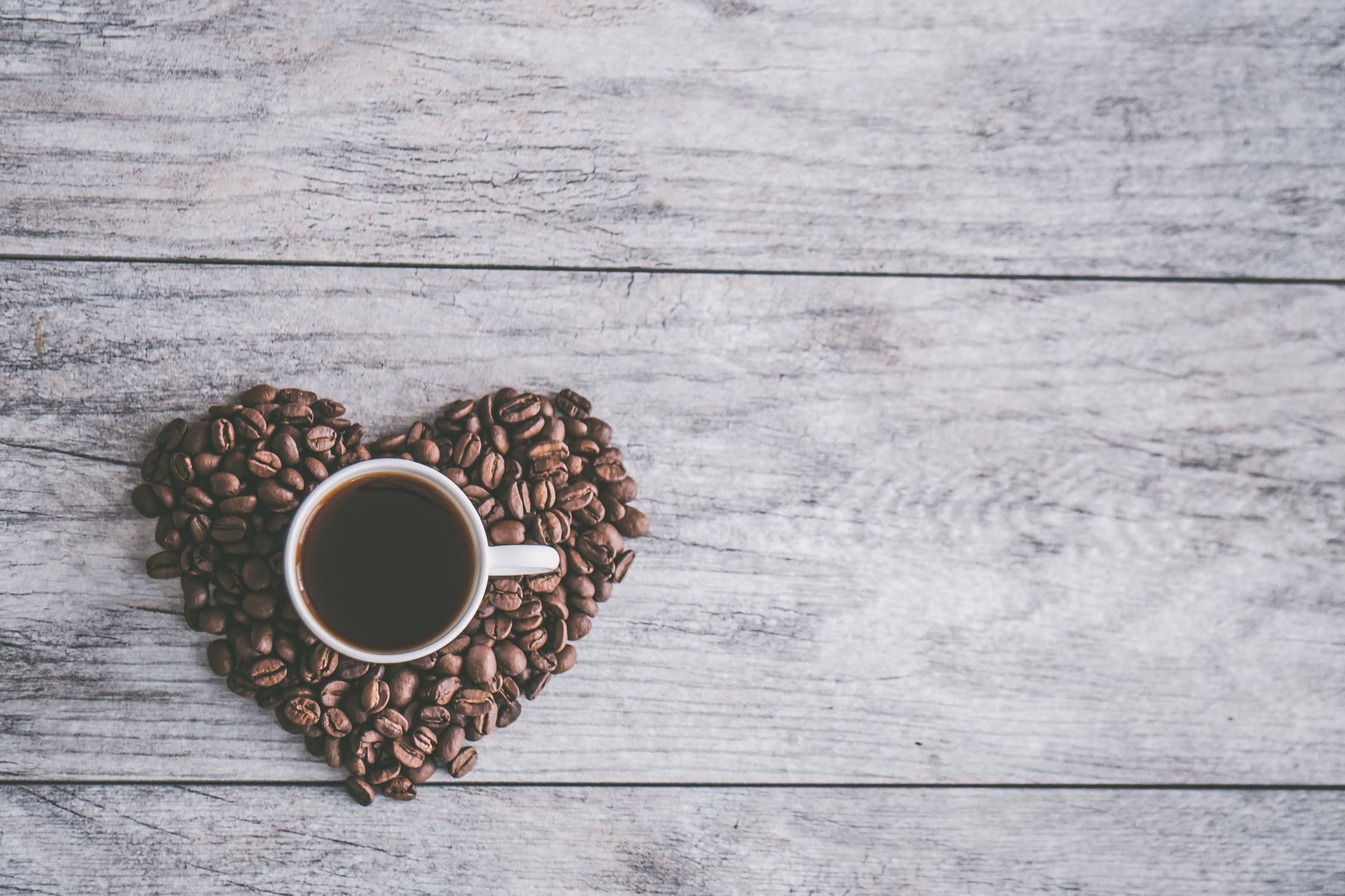 white ceramic mug filled with brown liquid on heart shaped coffee beans